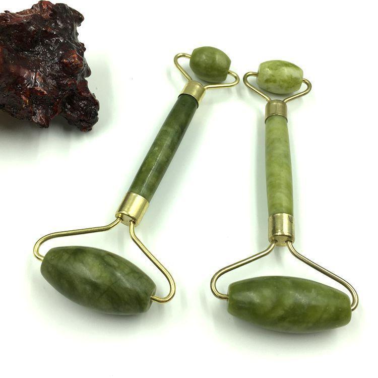 Two green Jade Facial Massage Rollers and a Gua Sha tool resting on a natural bamboo mat with small dried botanicals.